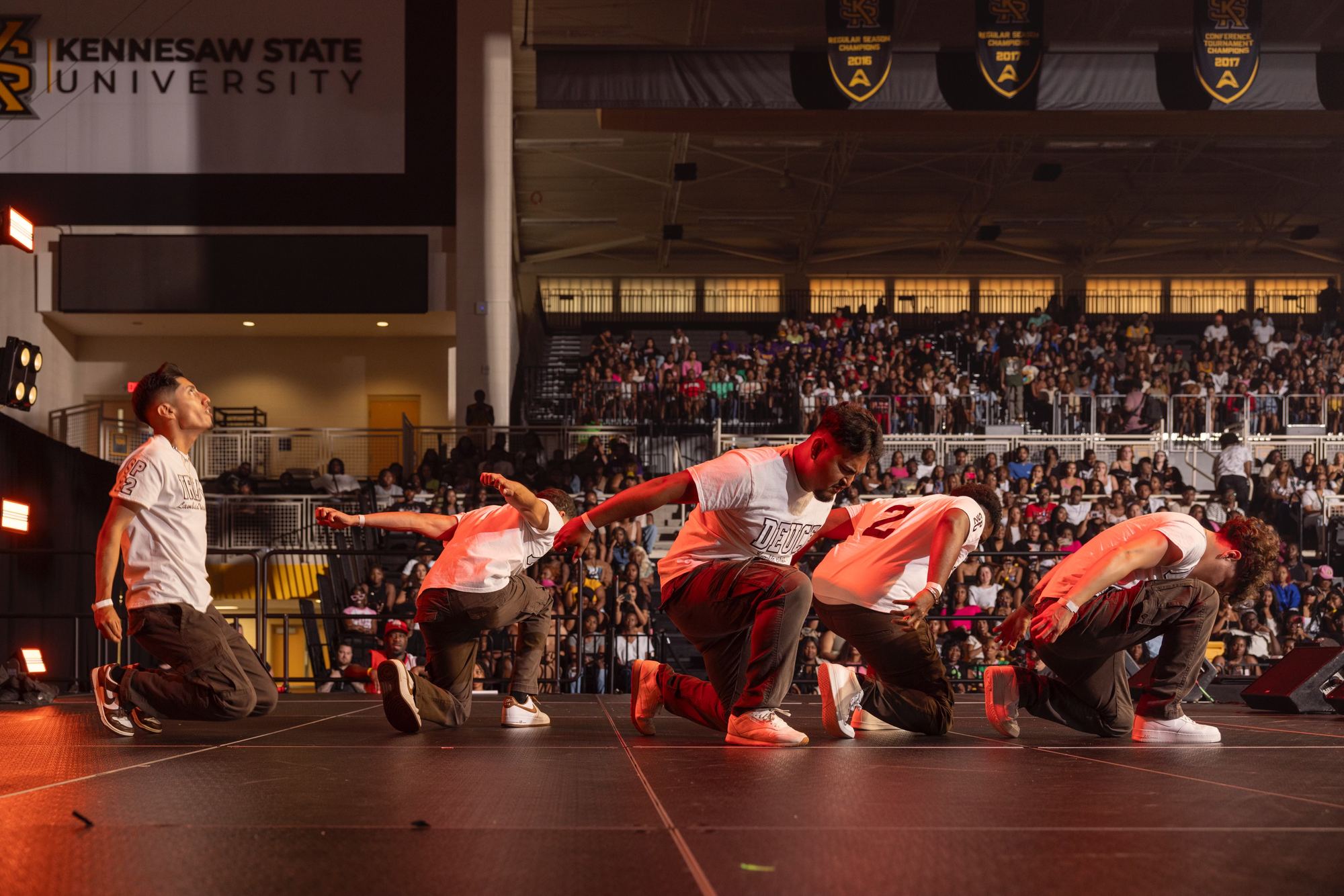 Five brothers mid-stroll on stage in front of a packed university arena.